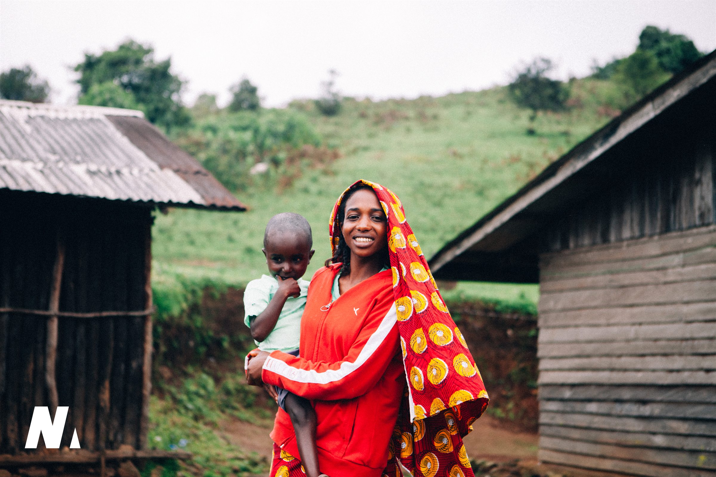 A smiling woman holding a young child between village buildings