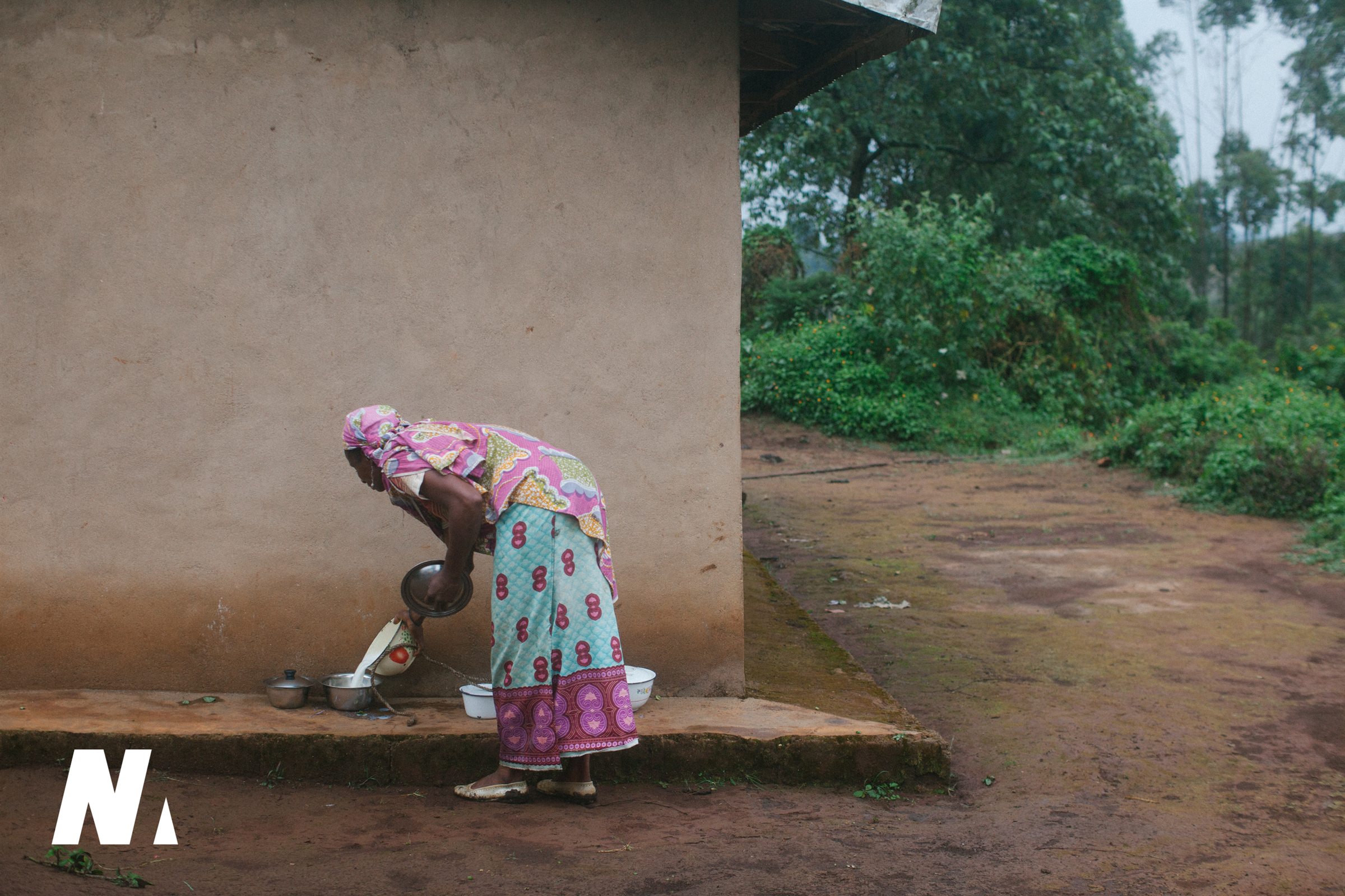 A woman pours water into bowls beside her home