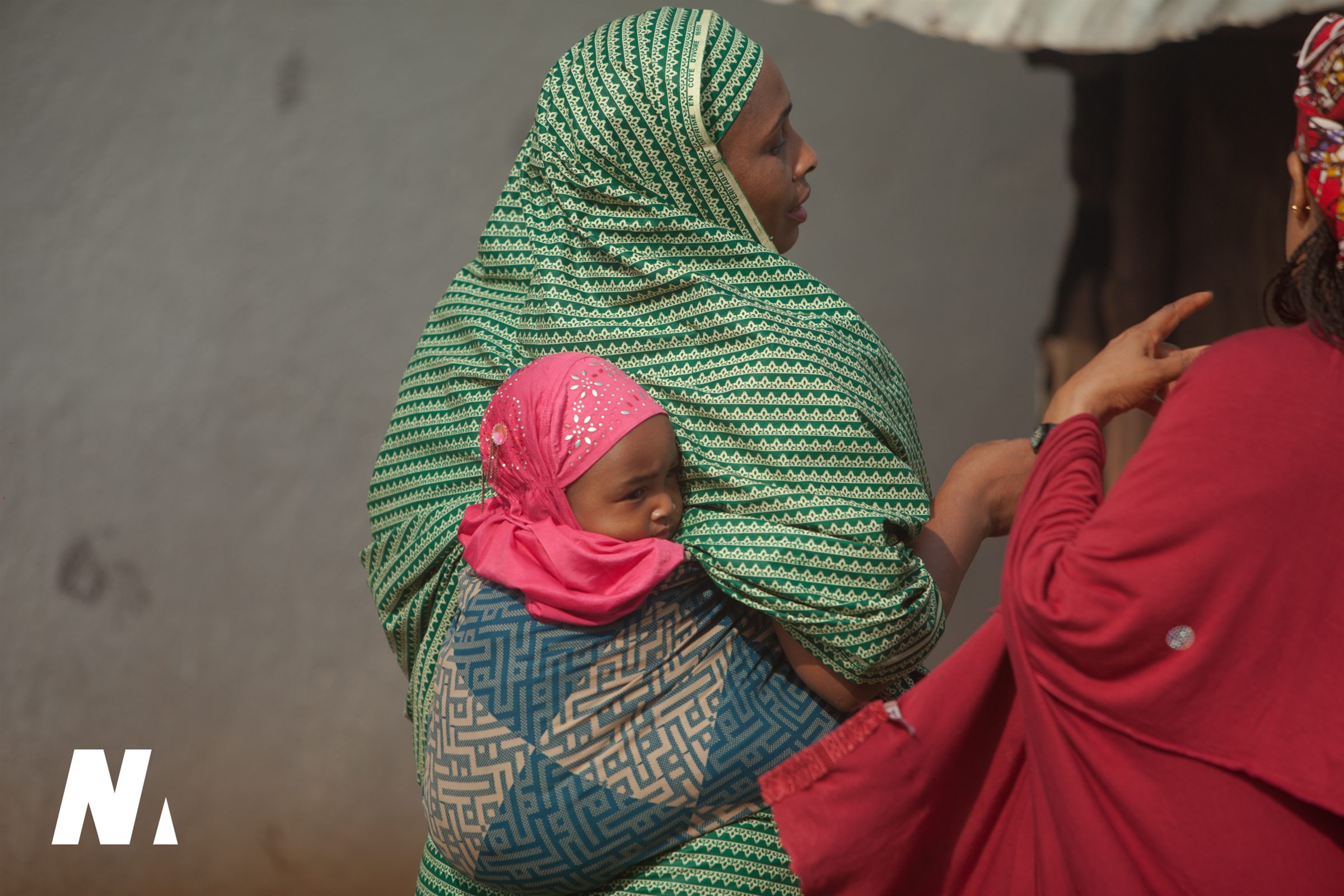 A baby wrapped close to a woman speaking with a neighbour