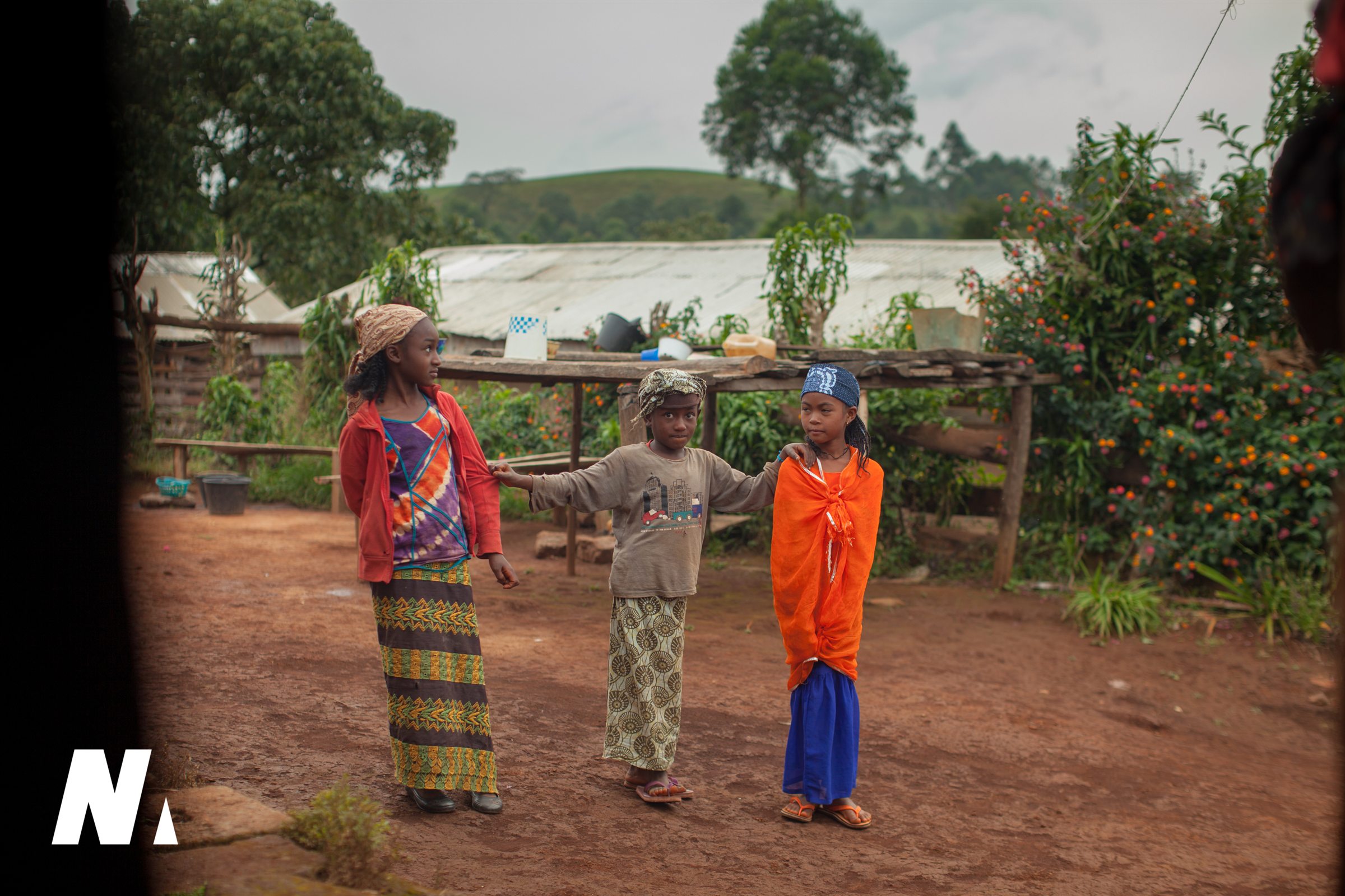 Three children standing together in a village yard