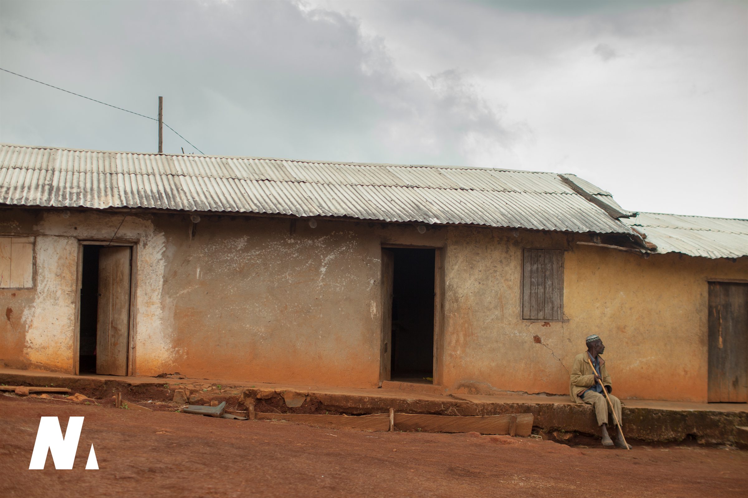 An older man seated outside a long earthen building